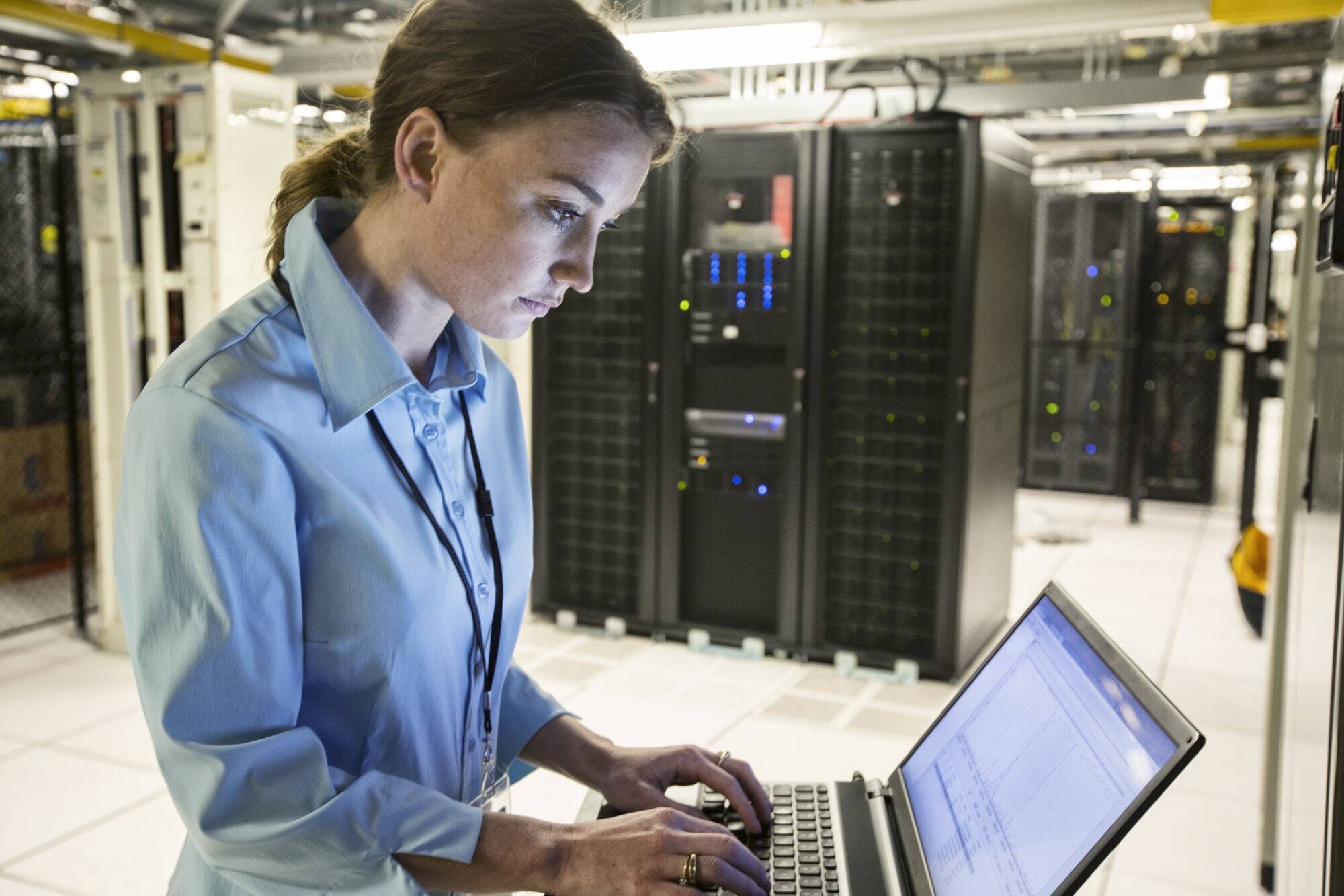 Caucasian woman technician running diagnostics on computer servers in a server farm.